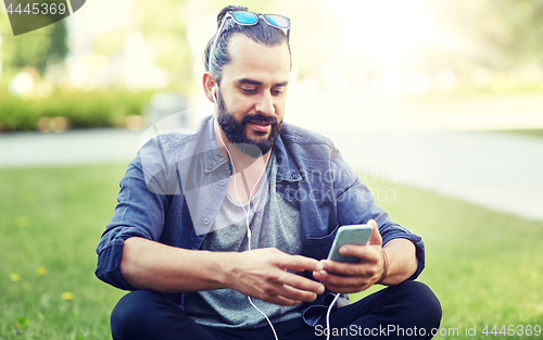 Image of man with earphones and smartphone sitting on grass