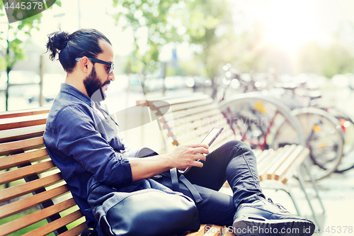 Image of man with tablet pc sitting on city street bench