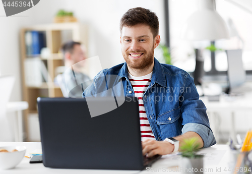 Image of smiling creative man with laptop working at office