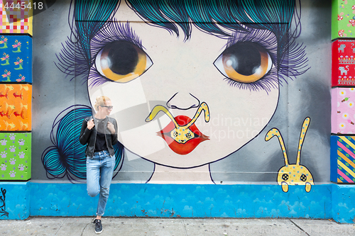 Image of Woman talking on smartphone leaning against colorful graffiti wall in New York city, USA.