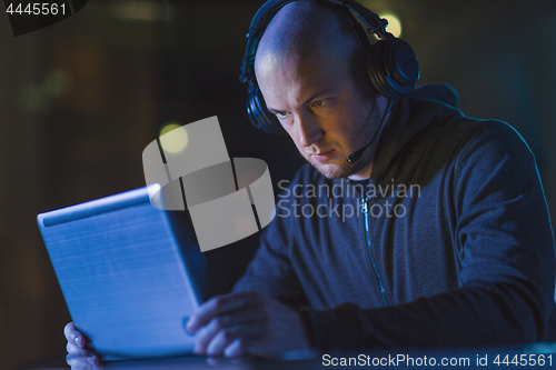 Image of hacker in headset typing on laptop in dark room