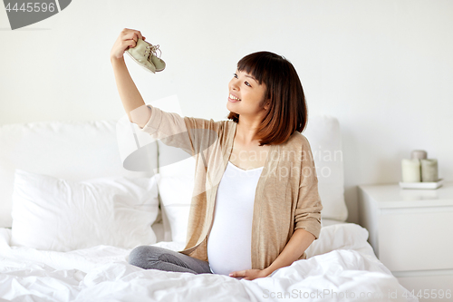 Image of happy pregnant woman with bootees in bed at home