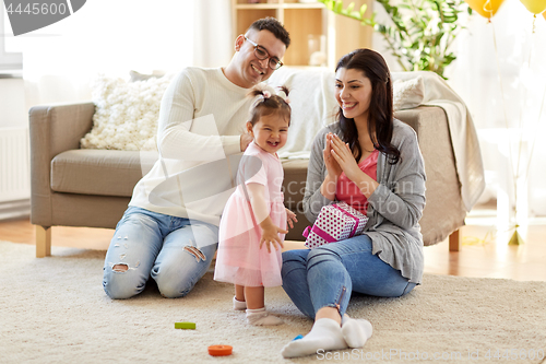 Image of baby girl with birthday gift and parents at home