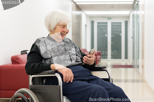 Image of Lonley elderly 95 years old woman sitting at the wheelchair using modern mobile phone.