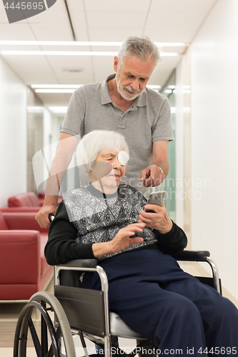 Image of Middle aged man showing and helping elderly 95 years old woman sitting at the wheelchair how to use modern mobile phone.