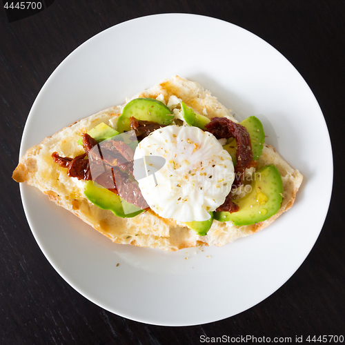 Image of Poached egg on a toasted bun with avocados and dried tomatoes.