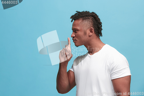 Image of The young afro-american man whispering a secret behind her hand over blue background