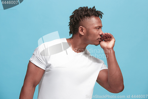 Image of The young afro-american man whispering a secret behind her hand over blue background