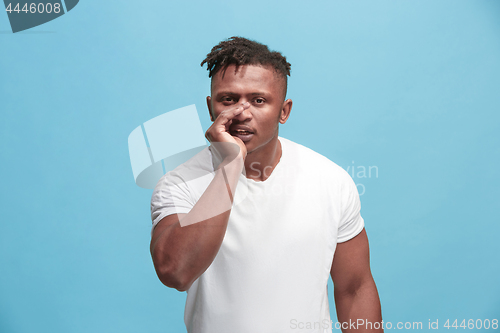 Image of The young afro-american man whispering a secret behind her hand over blue background