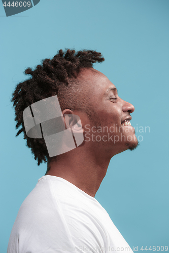 Image of The happy business Afro-American man standing and smiling against blue background. Profile view.