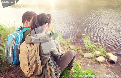 Image of couple with backpacks sitting on river bank