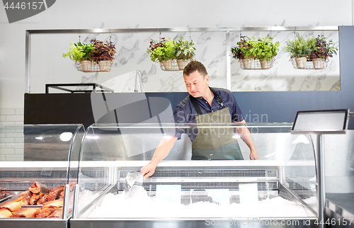 Image of male seller adding ice to fridge at fish shop