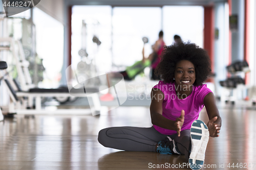 Image of woman in a gym stretching and warming up man in background worki