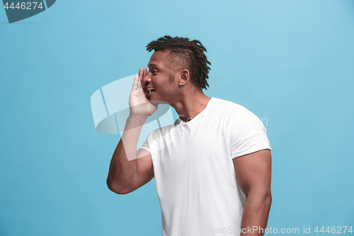 Image of The young afro-american man whispering a secret behind her hand over blue background