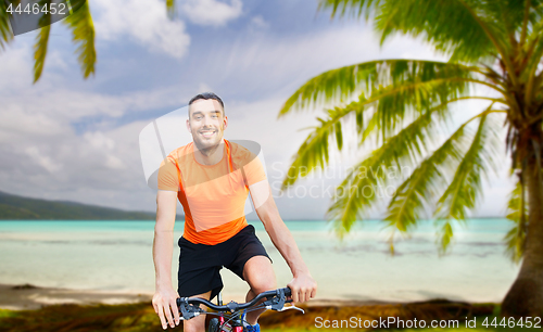 Image of happy young man riding bicycle over tropical beach