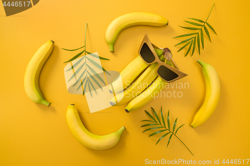 Image of Bananas, sunglasses and palm leaves on yellow background