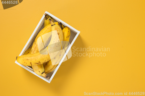 Image of Box of ripe bananas on vivid yellow background