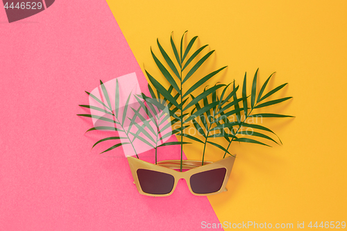 Image of Palm leaves and sunglasses on pink and yellow background