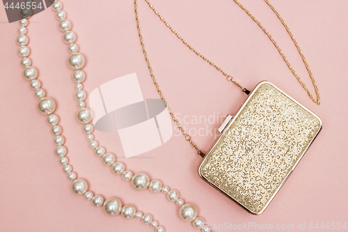 Image of Golden purse and pearl necklace on pink background