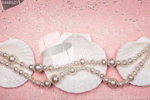 Image of Pearl necklace and seashells on glitter pink background