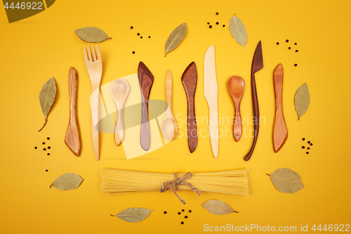 Image of Wooden utensils, pasta and spices on yellow background