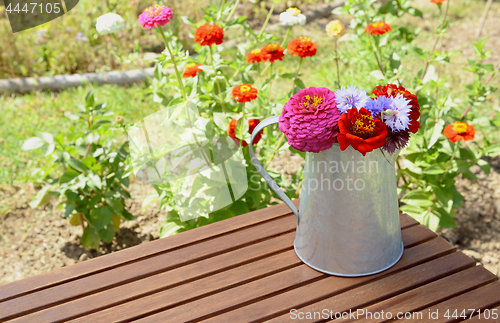 Image of Arrangement of zinnias and cornflowers in a metal jug outdoors
