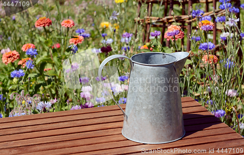 Image of Empty metal pitcher on a table in a flower garden