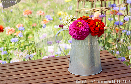 Image of Zinnias in a rustic pitcher on a garden table