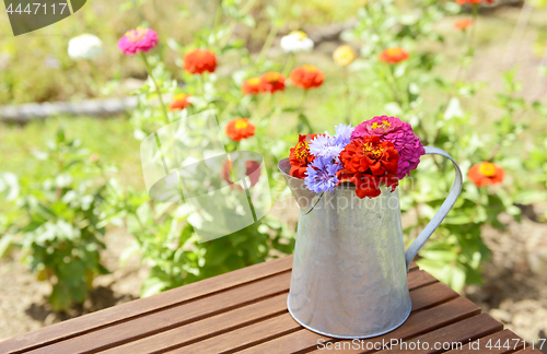 Image of Metal pitcher full of brightly coloured flowers