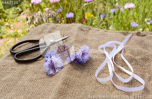 Image of Ribbon and scissors with freshly cut cornflowers on hessian