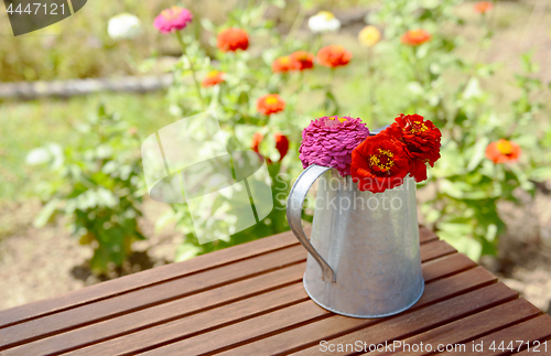 Image of Rustic pitcher holding zinnia flowers on a garden table