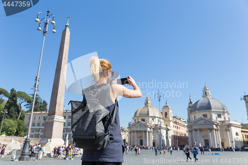 Image of Female tourist with a fashinable vintage hipster backpack taking photo of Piazza del Popolo in Rome, Italy by her mobile phone.