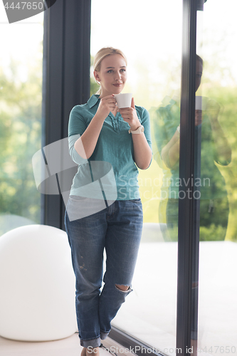 Image of young woman drinking morning coffee by the window