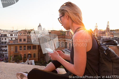 Image of Female tourist using mobile phone travel app close to Piazza di Spagna, landmark square with Spanish steps in Rome, Italy at sunset.