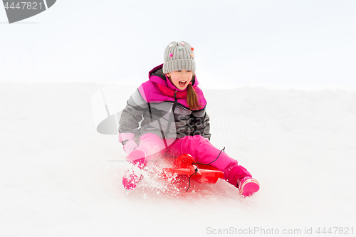 Image of happy little girl sliding down on sled in winter