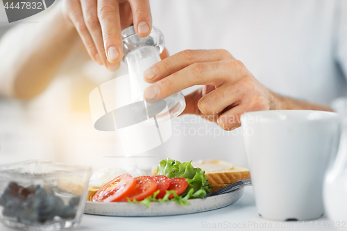 Image of close up of male hands seasoning food by salt mill