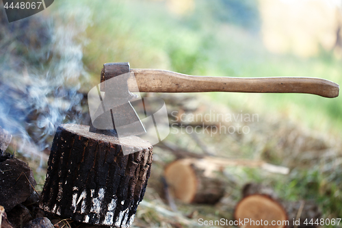 Image of Axe in tree stump and smoke from campfire