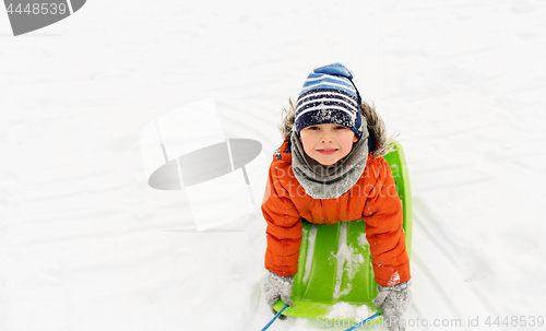 Image of happy little boy riding sled on snow in winter