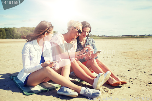 Image of group of happy women with smartphones on beach