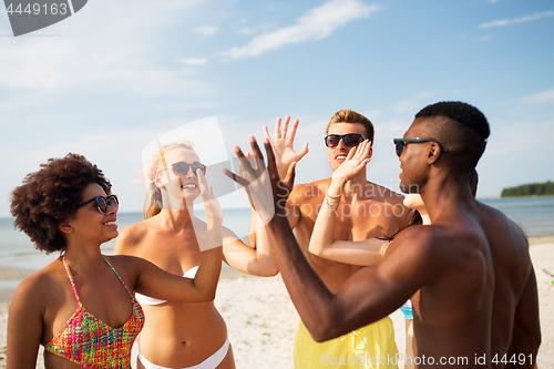 Image of happy friends making high five on summer beach