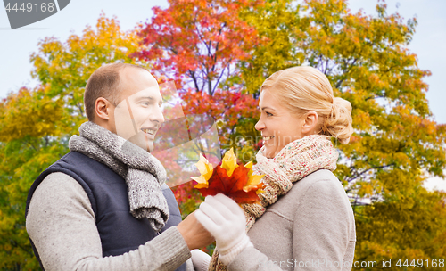 Image of smiling couple with maple leaves in autumn park