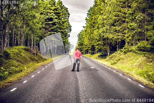 Image of Man in a red shirt looking down an asphalt road