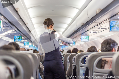 Image of Interior of commercial airplane with stewardess serving passengers on seats during flight.