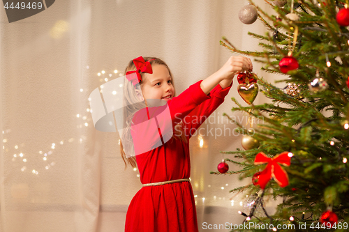 Image of happy girl in red dress decorating christmas tree