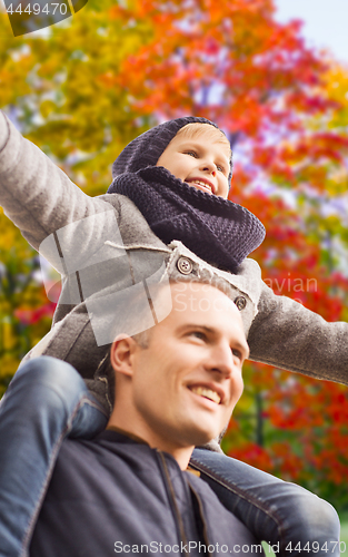 Image of happy father carrying son over autumn park 