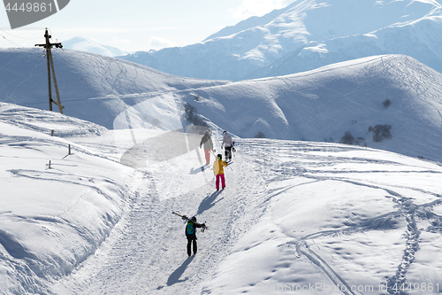 Image of Skiers and snowboarders on snow road at sun winter morning