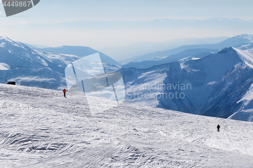 Image of Two skiers downhill on snow off-piste slope and mountains in haz