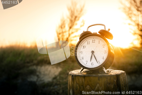 Image of Alarm clock on a wooden post in the morning sunrise