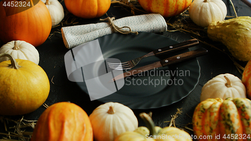 Image of Black plate and cutlery surrounded by pumpkins