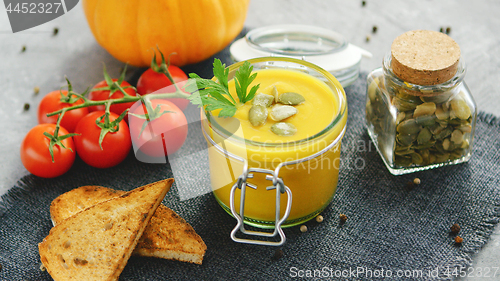 Image of Creamy pumpkin soup in jar with bread and tomatoes